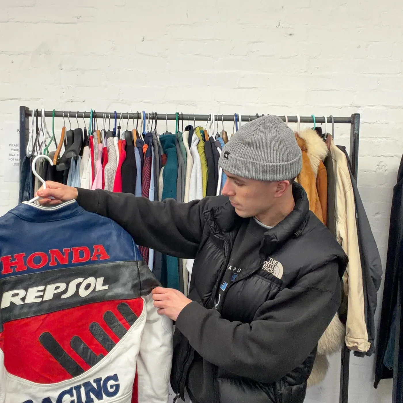 A Honda Repsol racing jacket held up in front of a rail of vintage coats and jackets